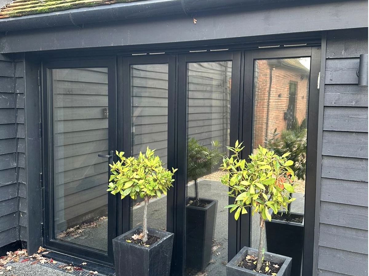 Solar film on black bi-fold doors, the glass reflecting the courtyard